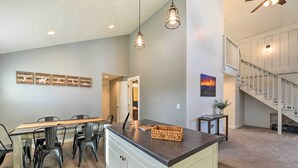 A modern kitchen with a central island, dining area with chairs, pendant lighting, and a staircase. - Centrally Located Pinedale Vacation Rental! (Pinedale)