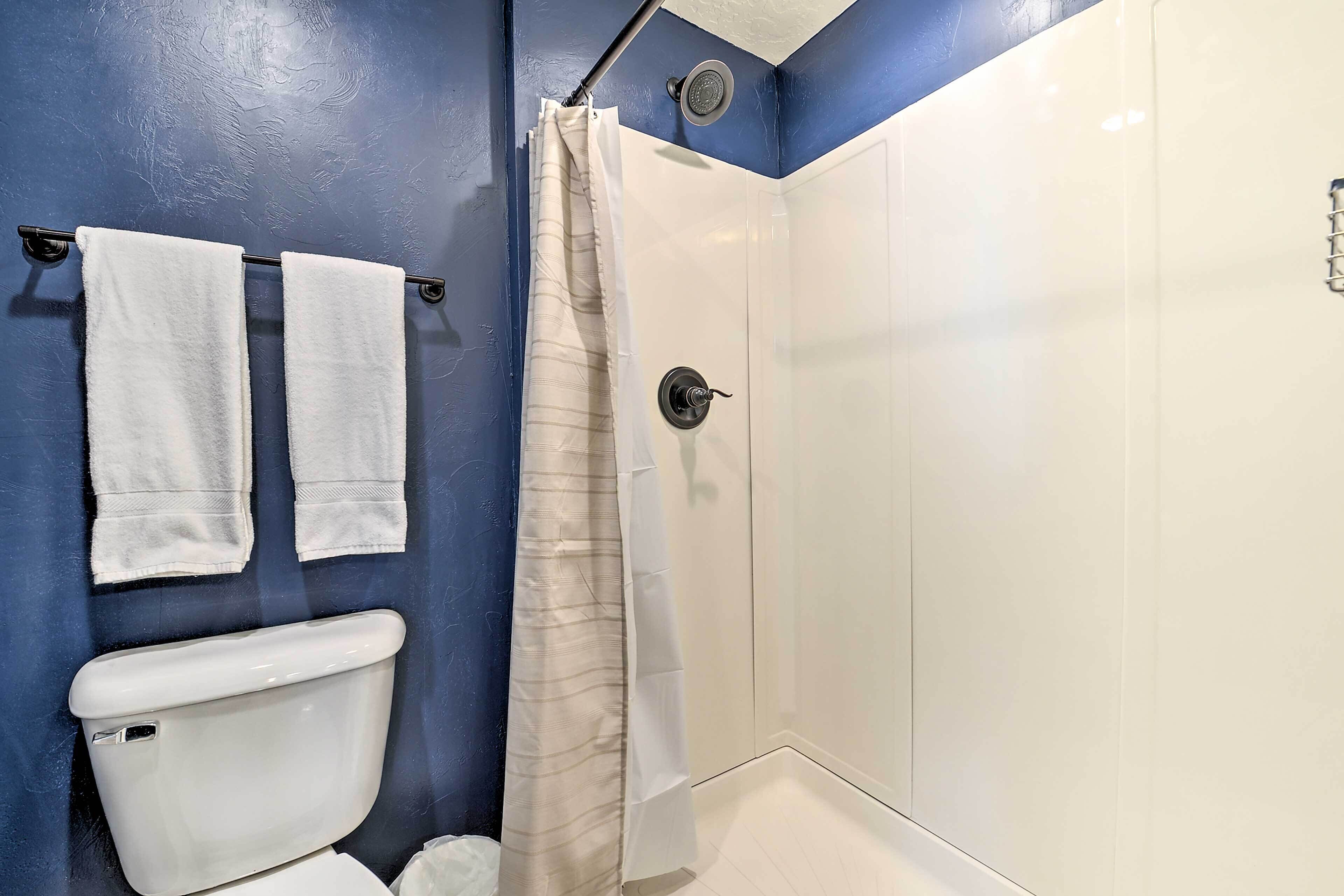 A bathroom with a toilet, two towels hanging on a rack, a shower curtain, and a white tiled shower enclosure.