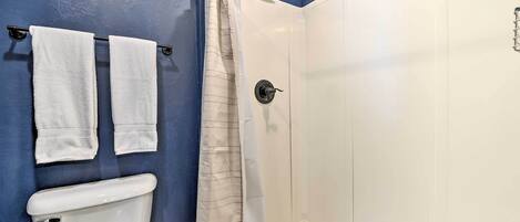 A bathroom with a toilet, two towels hanging on a rack, a shower curtain, and a white tiled shower enclosure.