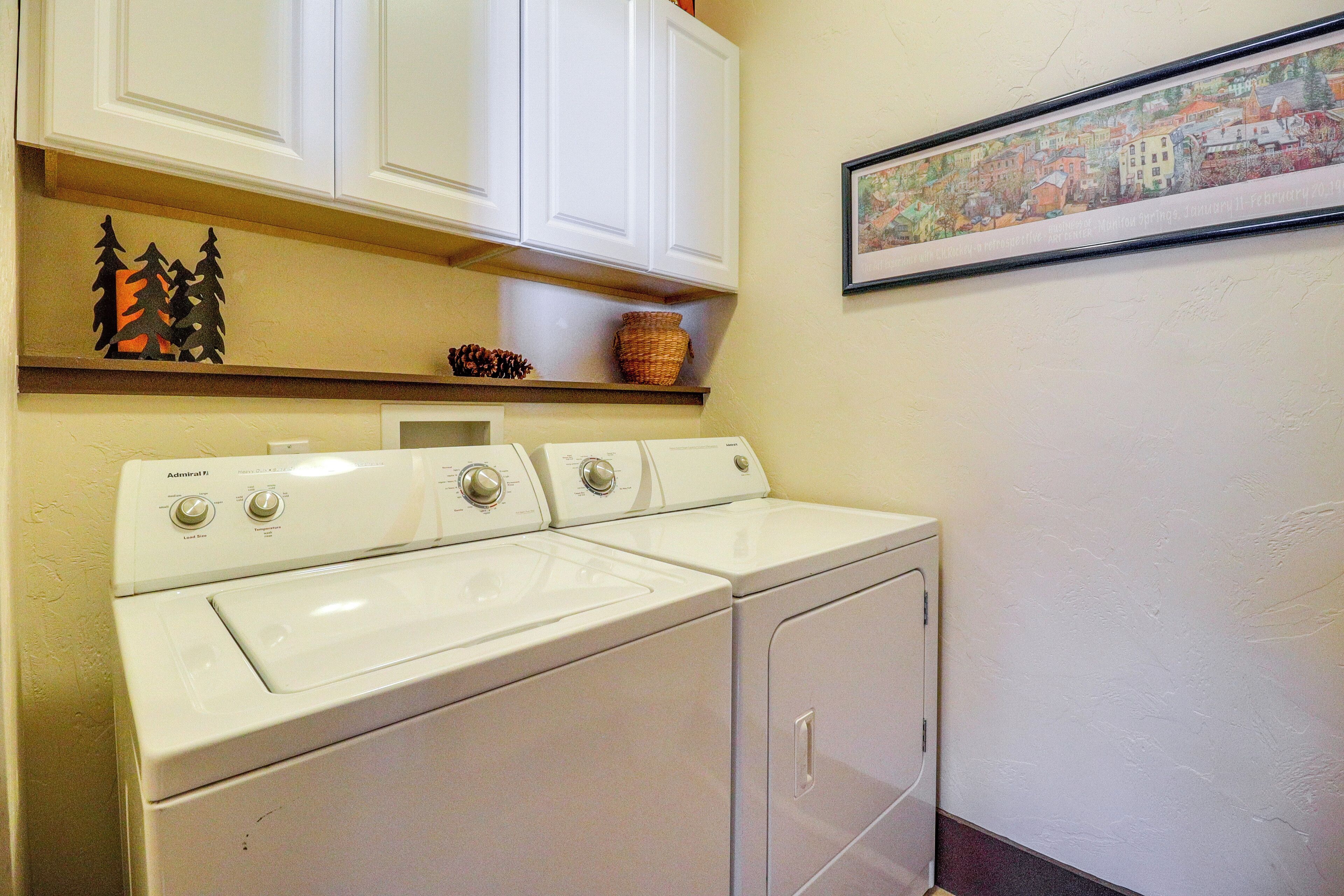 A laundry area with a front-loading washer and dryer, white cabinets above, and a framed picture on the wall.