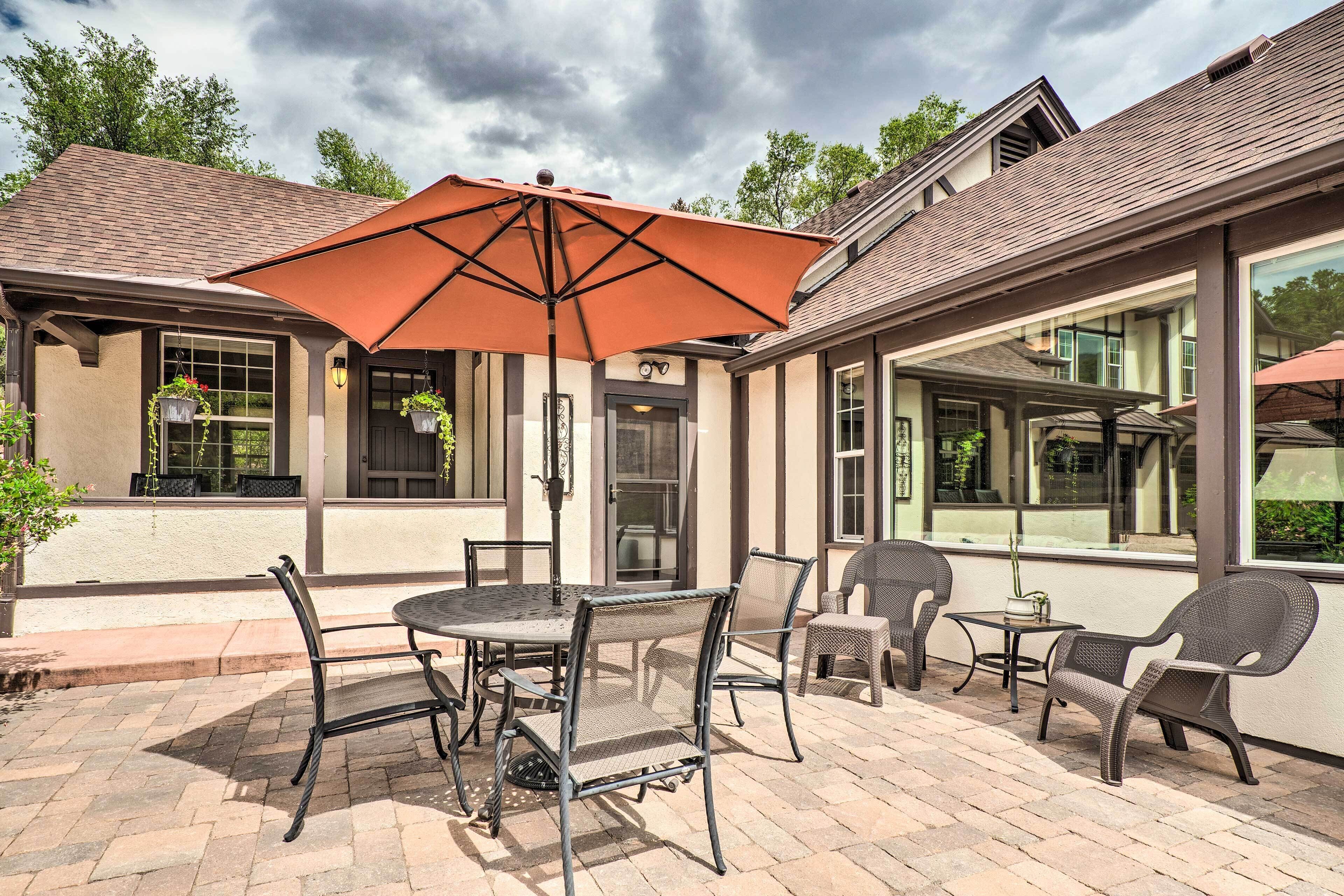 An outdoor patio with a round table and chairs, a large umbrella, and hanging planters.