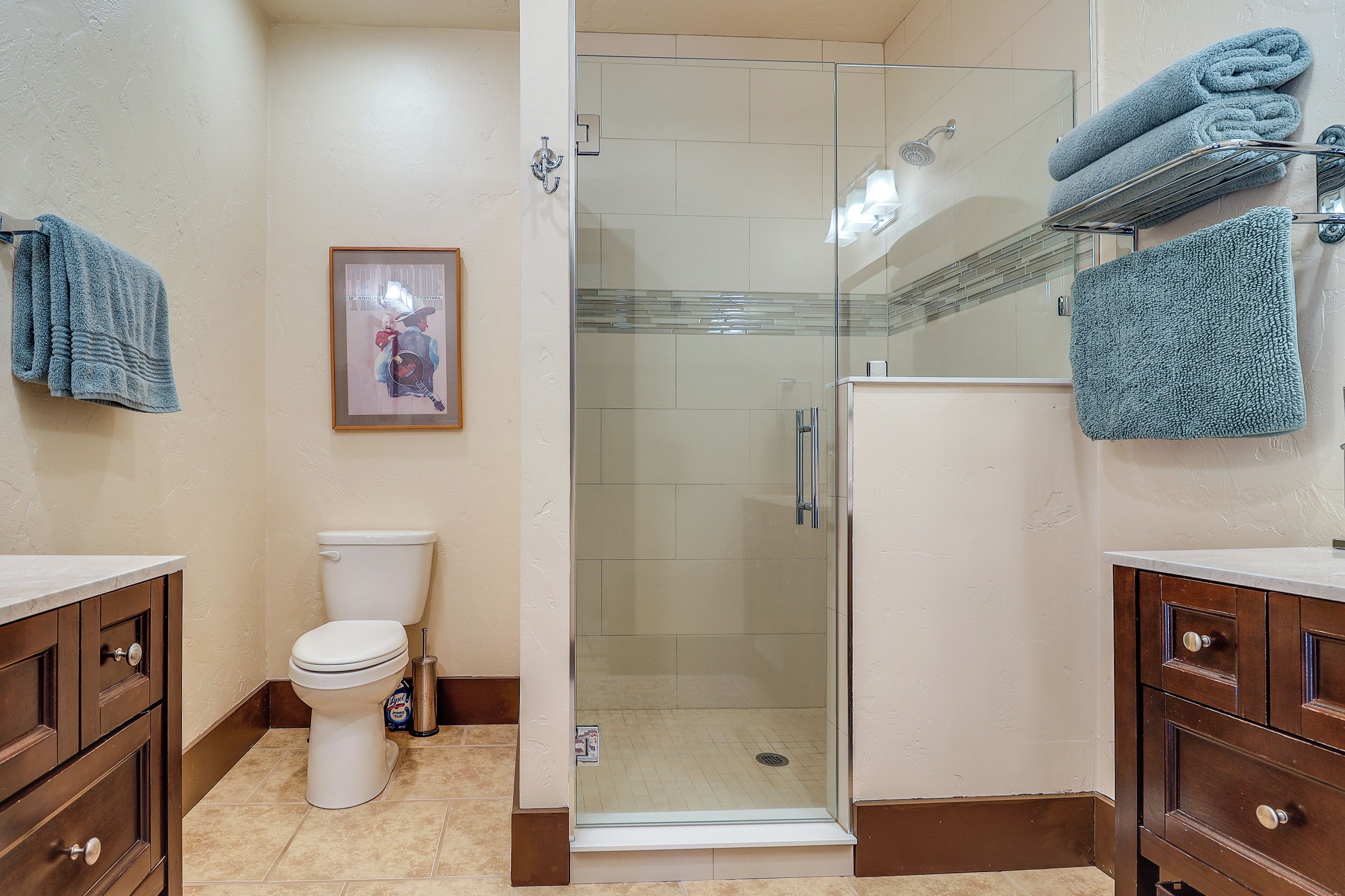 Een badkamer met een douchecabine van glas, een toilet en houten kastjes.
