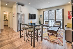 A modern kitchen with a stainless steel refrigerator, a dining table with stools, and a large window with a view of trees. - Traverse City Condo: Half Mi to Front Street! (Traverse City)