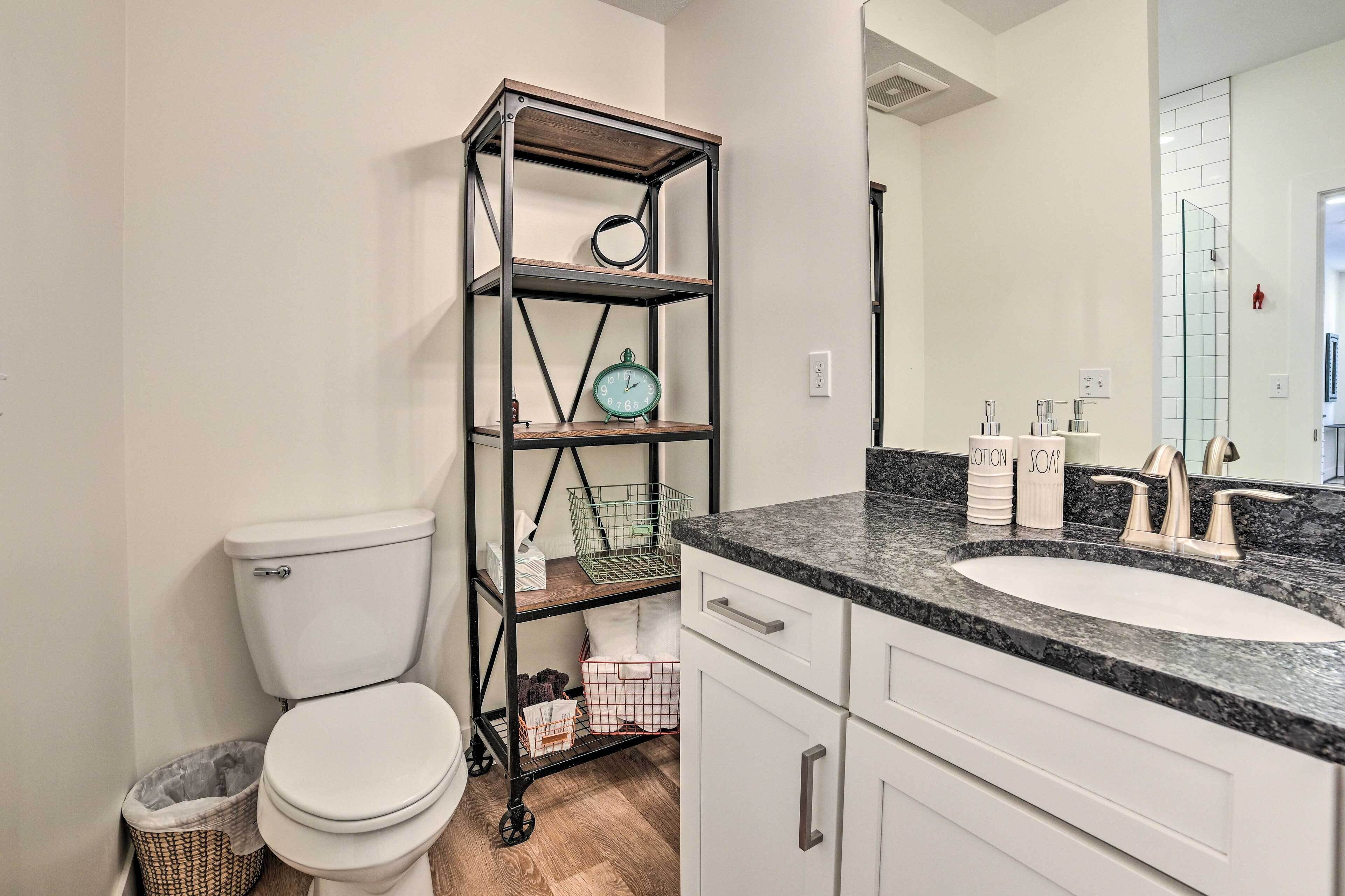 A bathroom with a toilet, a sink with a marble countertop, and a metal shelving unit with various items.