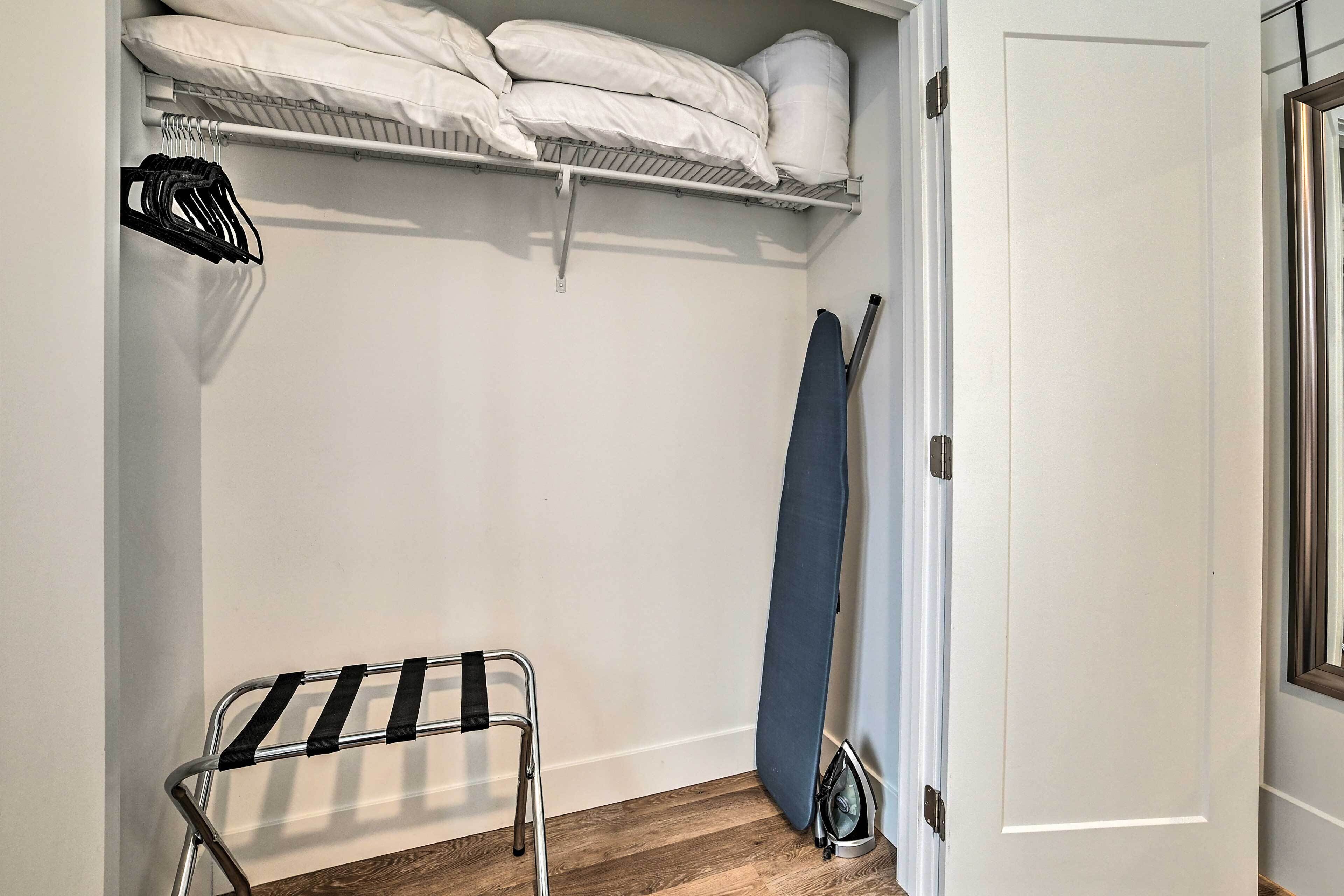 A small, neatly organized laundry room with a drying rack, ironing board, and shelves with folded linens.