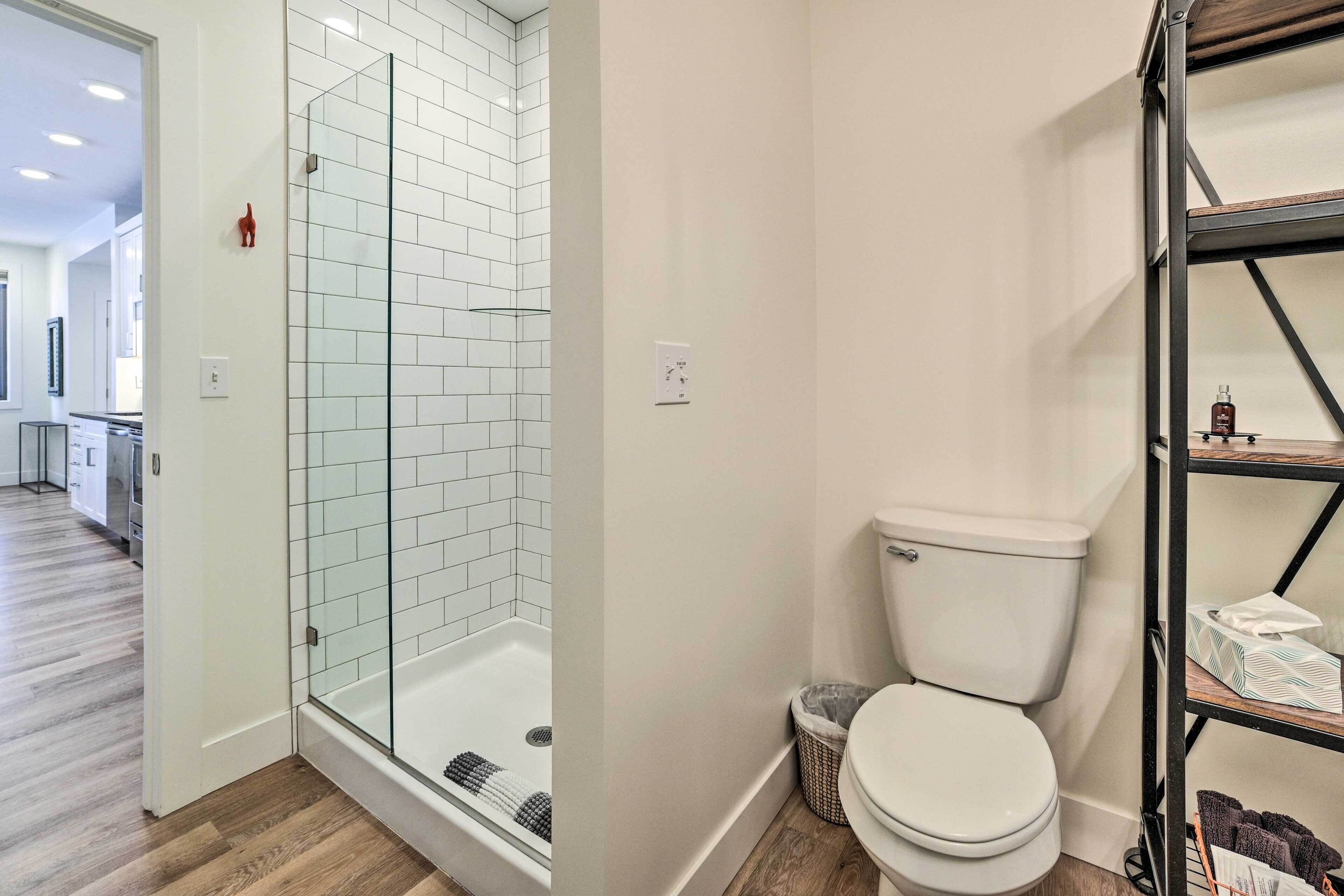 Et moderne badeværelse med brusekabine i glas, et hvidt toilet og trægulv.