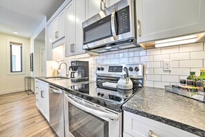A modern kitchen with stainless steel appliances, white cabinetry, and a granite countertop. - Traverse City Condo: Half Mi to Front Street! (Traverse City)