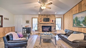 A living room with a stone fireplace, leather sofas, a glass coffee table, and a ceiling fan.