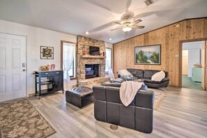 A living room with a stone fireplace, a ceiling fan, a black leather sofa, and a wooden wall panel.