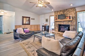 A living room with a stone fireplace, leather sofas, a glass coffee table, and a ceiling fan.