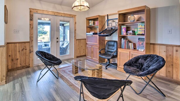 A room with a glass coffee table, two black lounge chairs, a wooden bookshelf, and a chandelier.