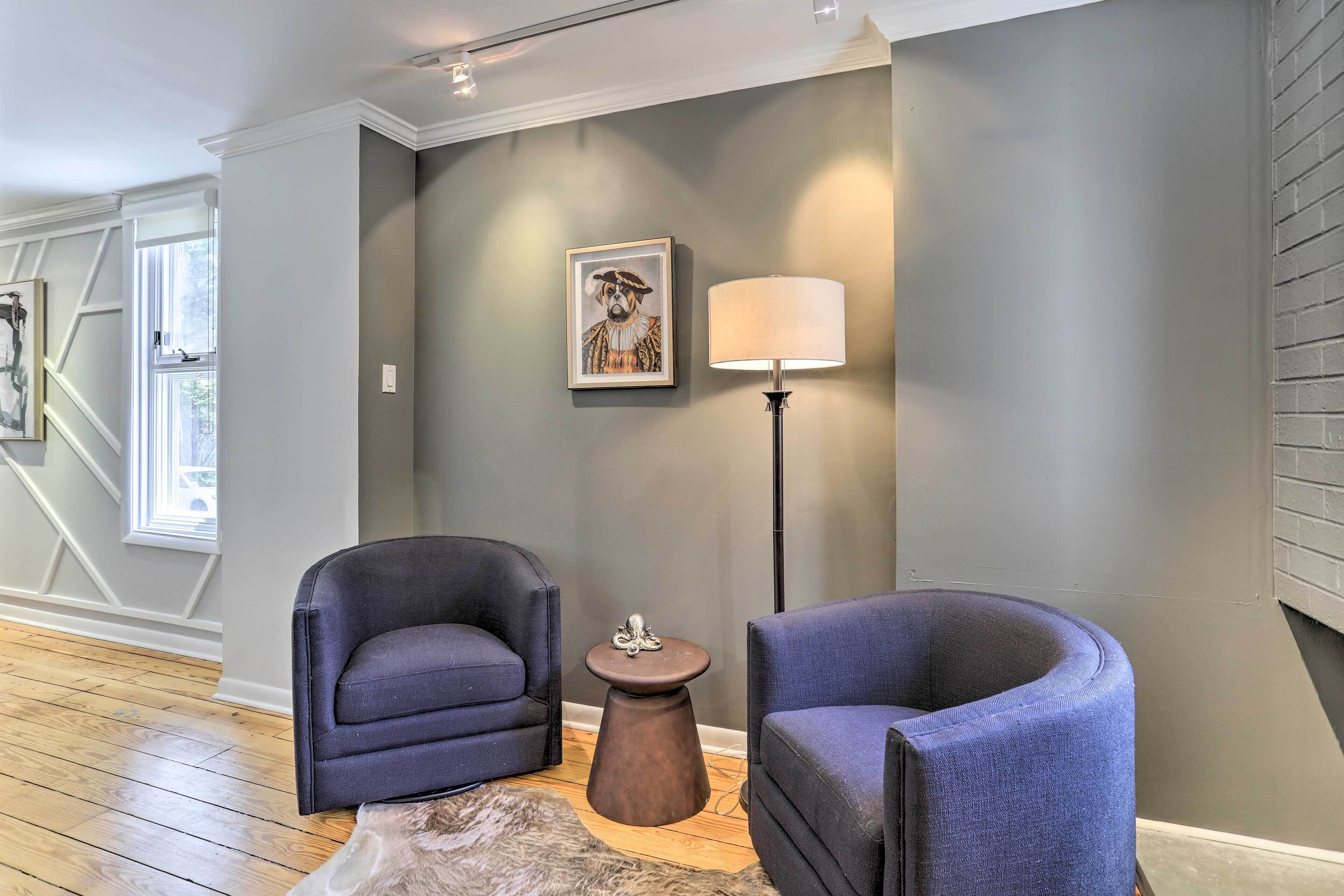 A room with two dark blue armchairs, a small round table, a floor lamp, and a framed picture on the wall.
