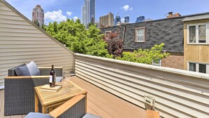 A rooftop patio with a wicker sofa, a wooden table, and a bottle of wine.