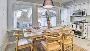 A modern kitchen with white cabinets, a stainless steel stove, and a dining area with a wooden table and chairs.