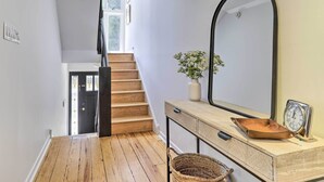 A staircase with wooden steps leading to a door, a mirror on the wall, a vase with flowers, and a clock on a table.