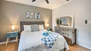 A bedroom with a bed, nightstand, dresser, ceiling fan, and artwork on the wall.