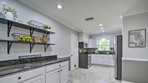 A modern kitchen with white cabinets, granite countertops, and a fruit basket on the wall.