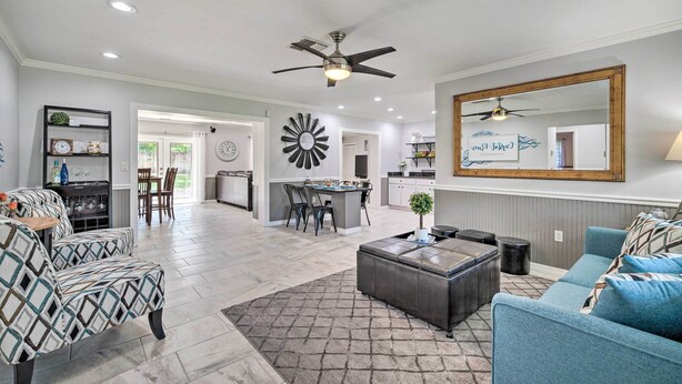 A spacious living room with a large mirror, a ceiling fan, and a dining area in the background.
