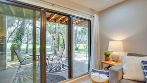 A room with a sliding glass door leading to an outdoor patio with a table and chairs. There is a sofa with a lamp and a basket of towels. - Seabrook Island Golf Resort Condo Near Beach! (Seabrook Island)
