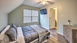 Ein Schlafzimmer mit einem Bett, einem Deckenventilator, einem an der Wand montierten Fernseher und einer Tür zu einem weiteren Raum.