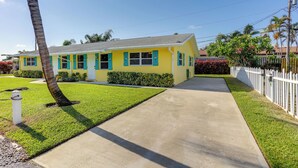 A yellow house with teal shutters, a concrete driveway, and a white picket fence. - 2 Mi to Swim & Shop: Updated North Palm Beach Home (Juno Beach)