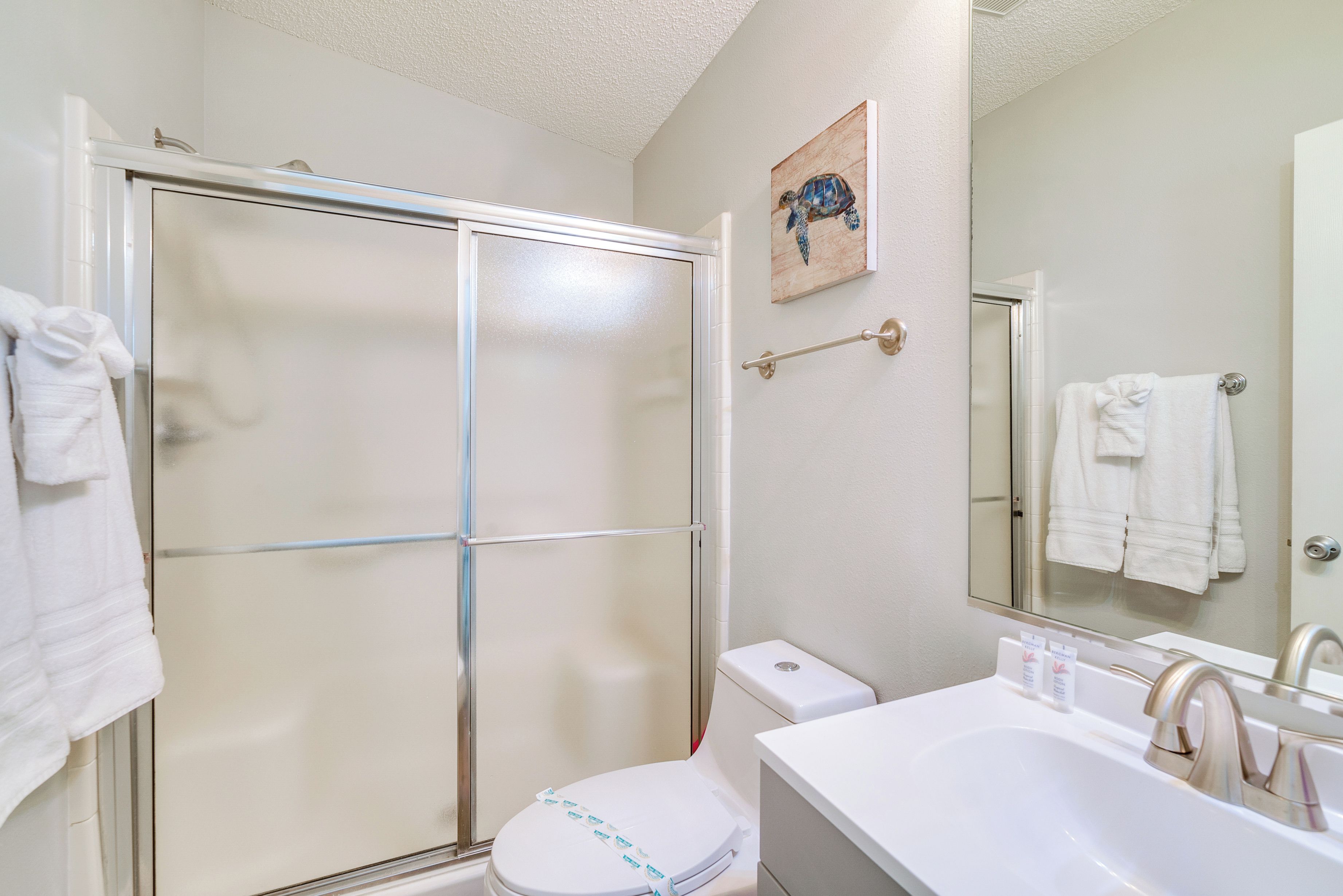 Een badkamer met een glazen douchecabine, toilet in het wit, een wastafel met spiegel en een handdoekrek.