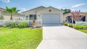 A single-story house with a garage, a front yard with a white picket fence, and a palm tree. - The Villages 2BR Vacation Home, Lanai & Golf Cart (The Villages)