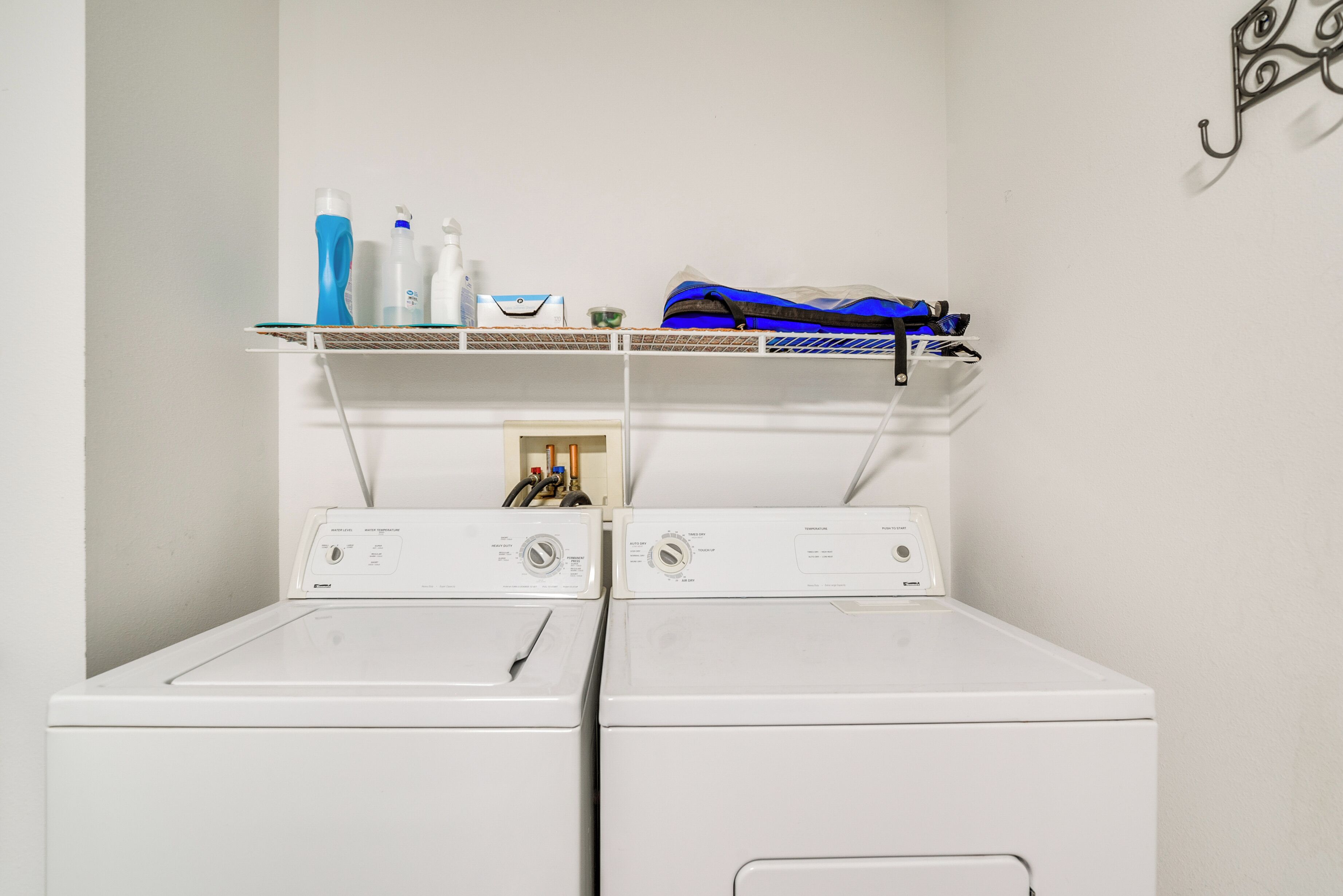 A laundry area with two white washing machines, a shelf with cleaning supplies, and a hanging bag.