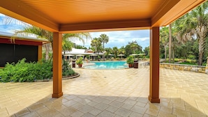 A covered outdoor area with a pool, palm trees, and a tiled floor. - The Villages 2BR Vacation Home, Lanai & Golf Cart (The Villages)