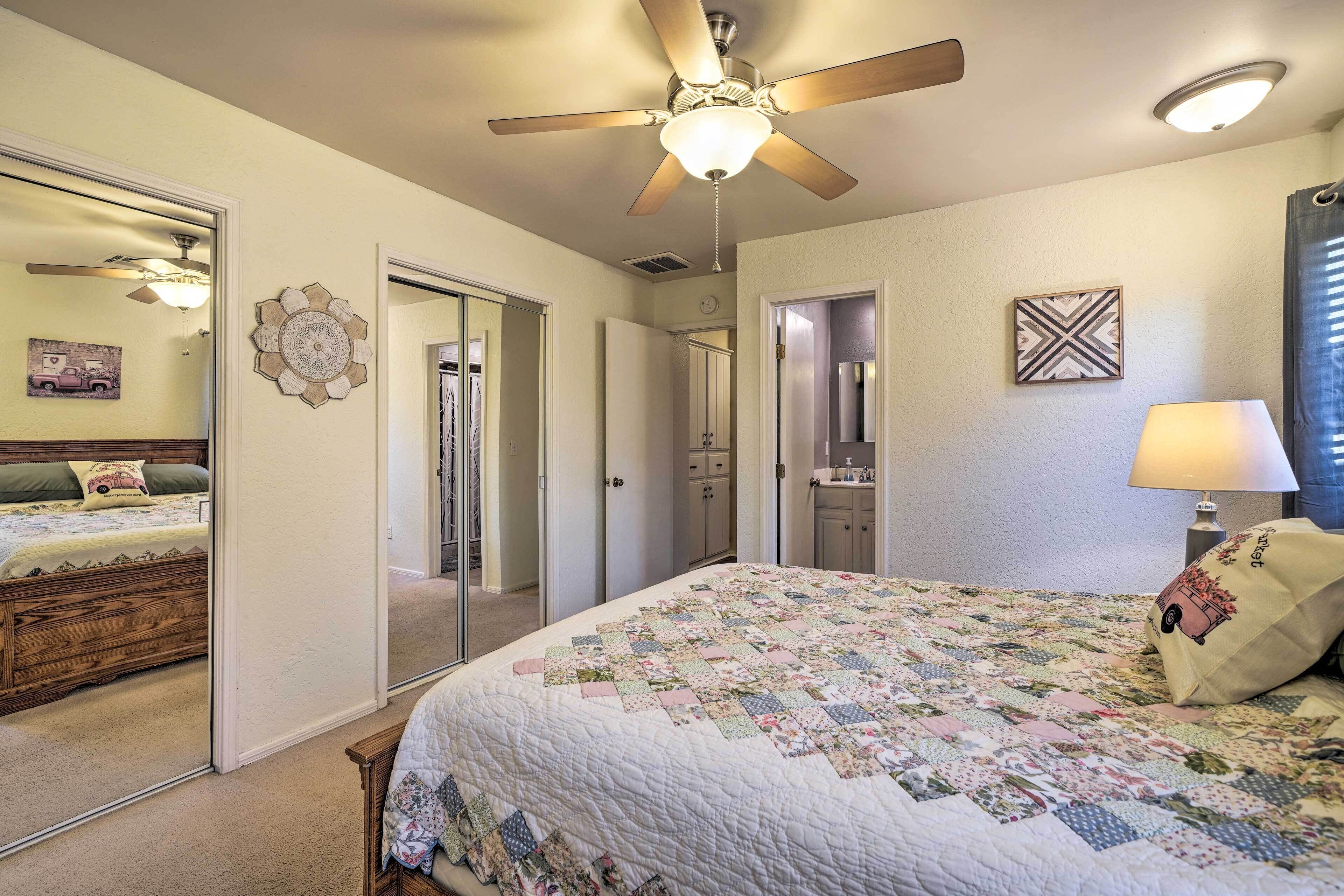 A bedroom with a large bed, a ceiling fan, a mirror, and a dresser.