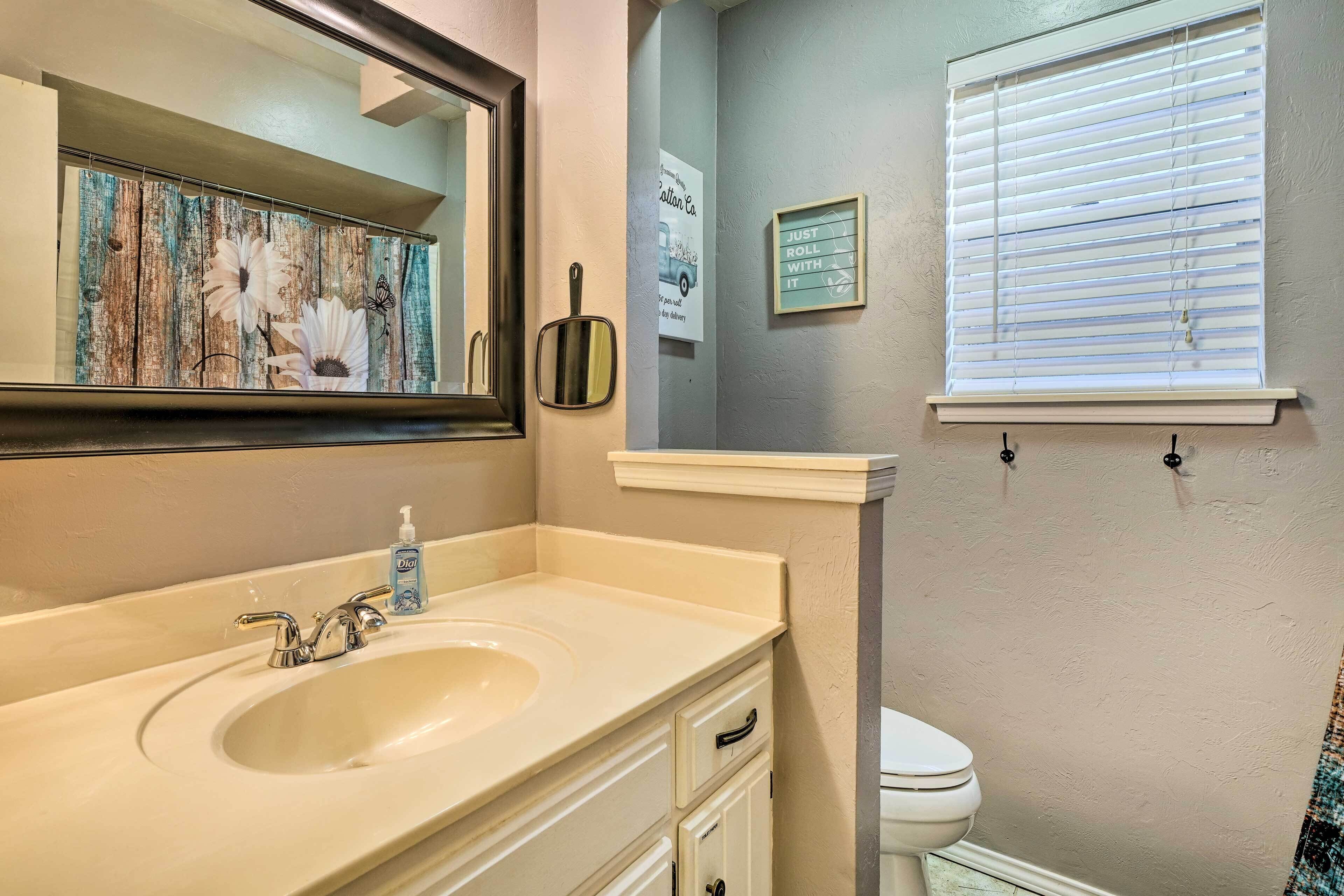 A bathroom with a sink, mirror, toilet, and window with blinds.