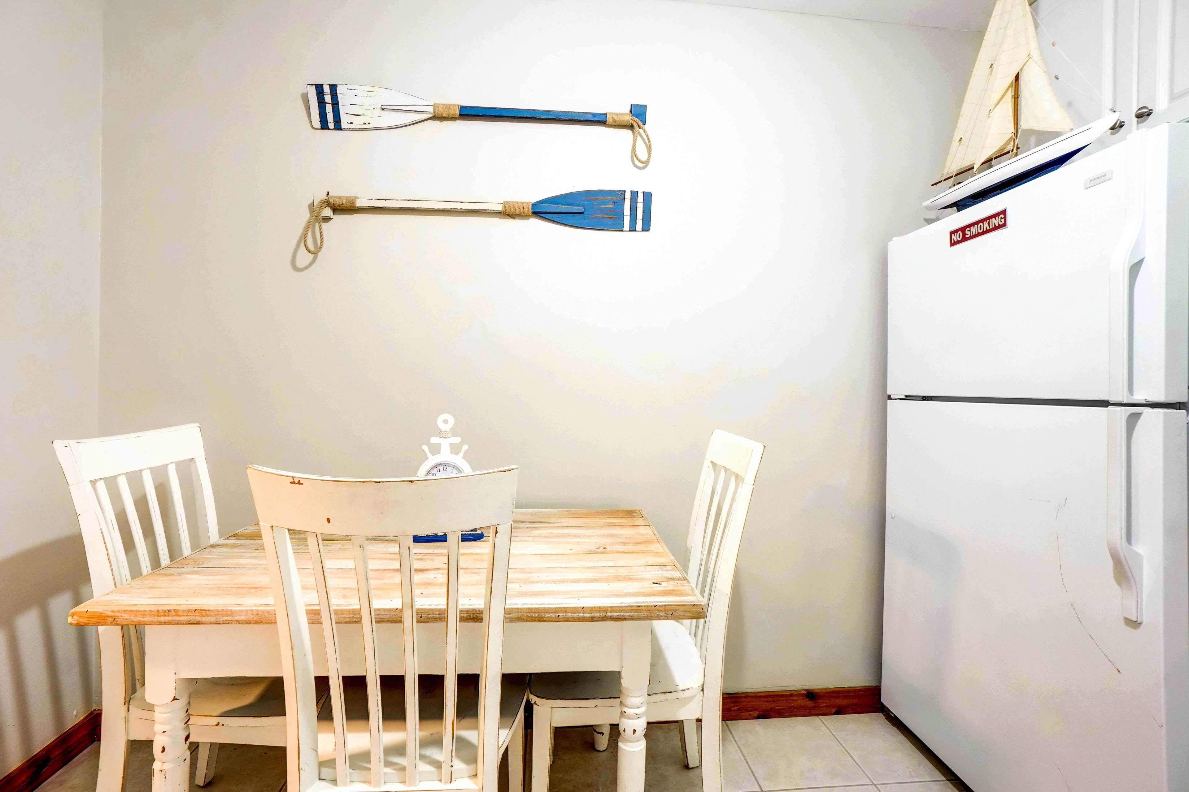 Un'area pranzo di piccole dimensioni con tavolo in legno e sedie bianche, un frigorifero bianco e un modellino di barca a vela appeso al muro.