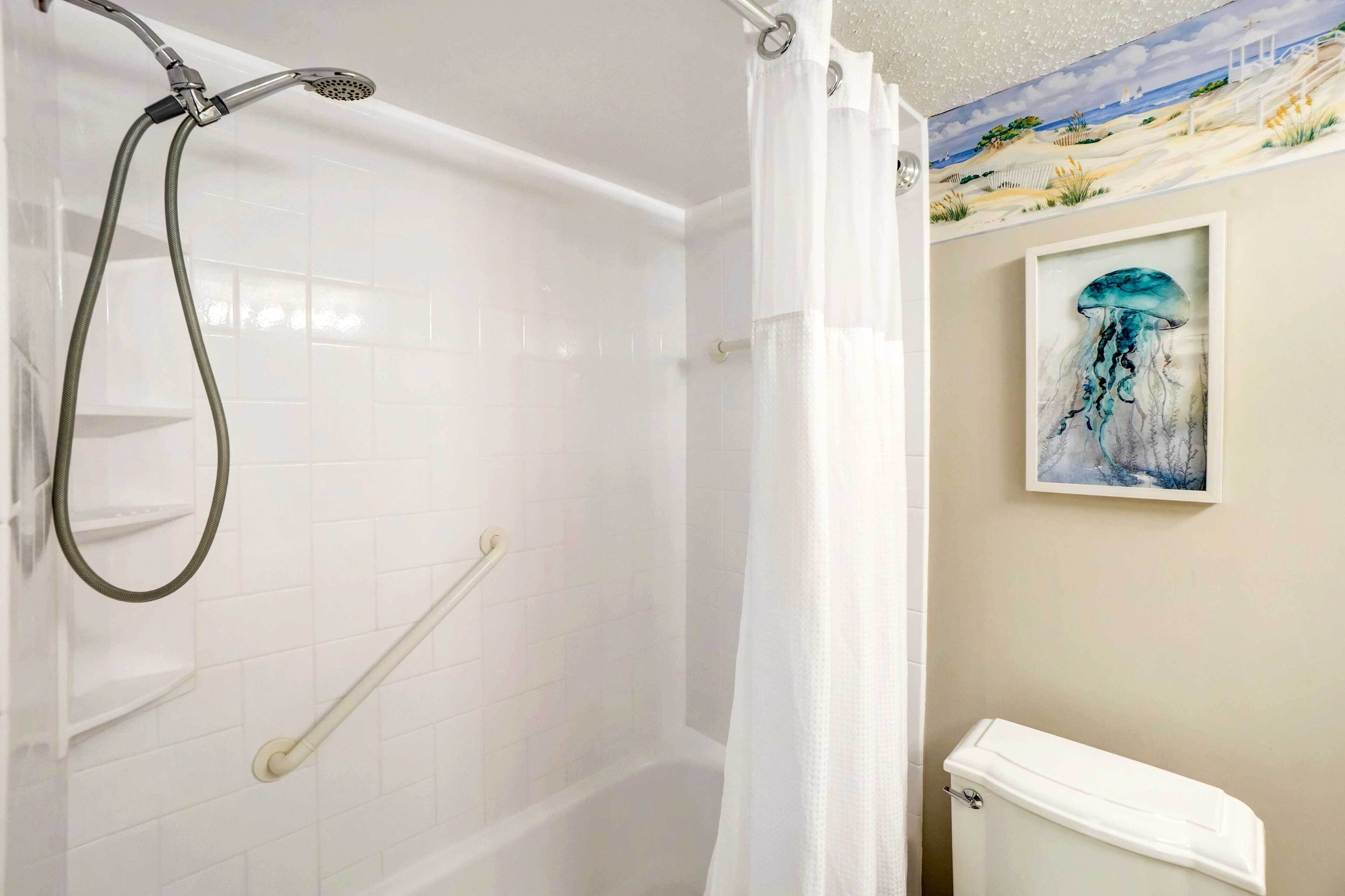 A shower with a handheld showerhead and a handheld shower attachment, a white toilet, and a framed artwork of a jellyfish on the wall.