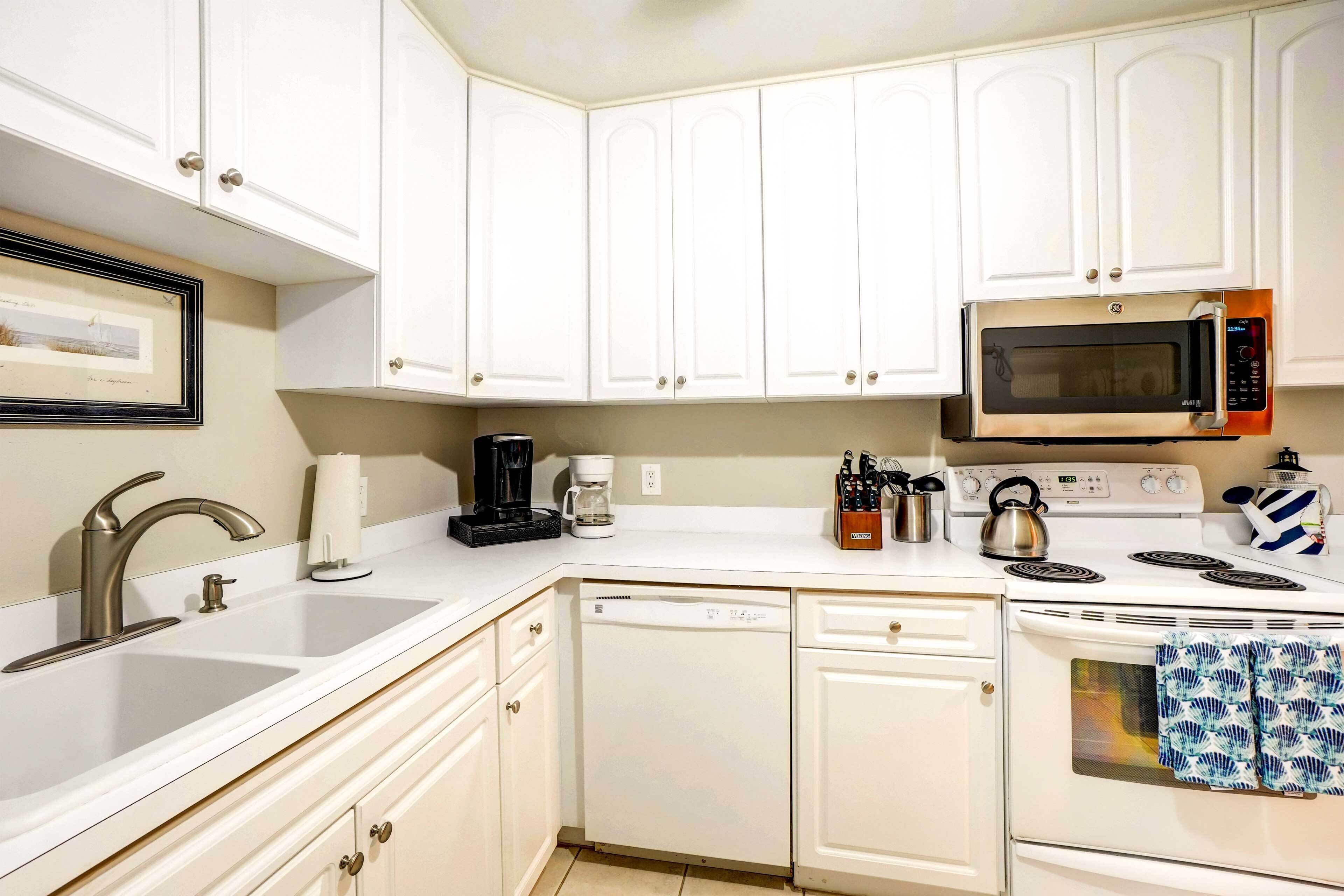 A kitchen with white cabinets, a stainless steel microwave, a coffee maker, and a dishwasher.