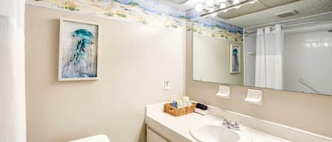 A bathroom with a sink, mirror, and toilet. There is a painting of a jellyfish on the wall and a beach scene above the mirror.