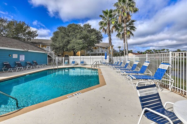 A pool area with blue and white lounge chairs, a pool with a 3 FT depth marker, and a white fence.