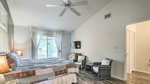 Quarto com cama grande, ventoinha no teto, televisão, janela com cortinas e porta.