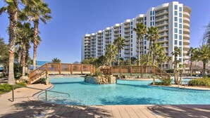 A resort with a large pool, palm trees, and a multi-story building in the background. - Modern Resort Condo With Balcony - Walk to Beach! (Destin)