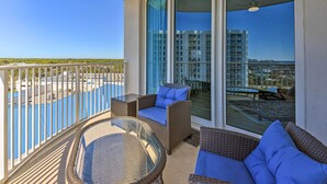 A balcony with wicker furniture, a glass table, and a view of a pool and buildings. - Modern Resort Condo With Balcony - Walk to Beach! (Destin)