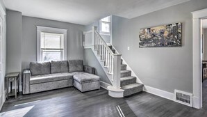 Un salon moderne avec un canapé d’angle gris, un escalier blanc et un tableau représentant un paysage urbain accroché au mur.
