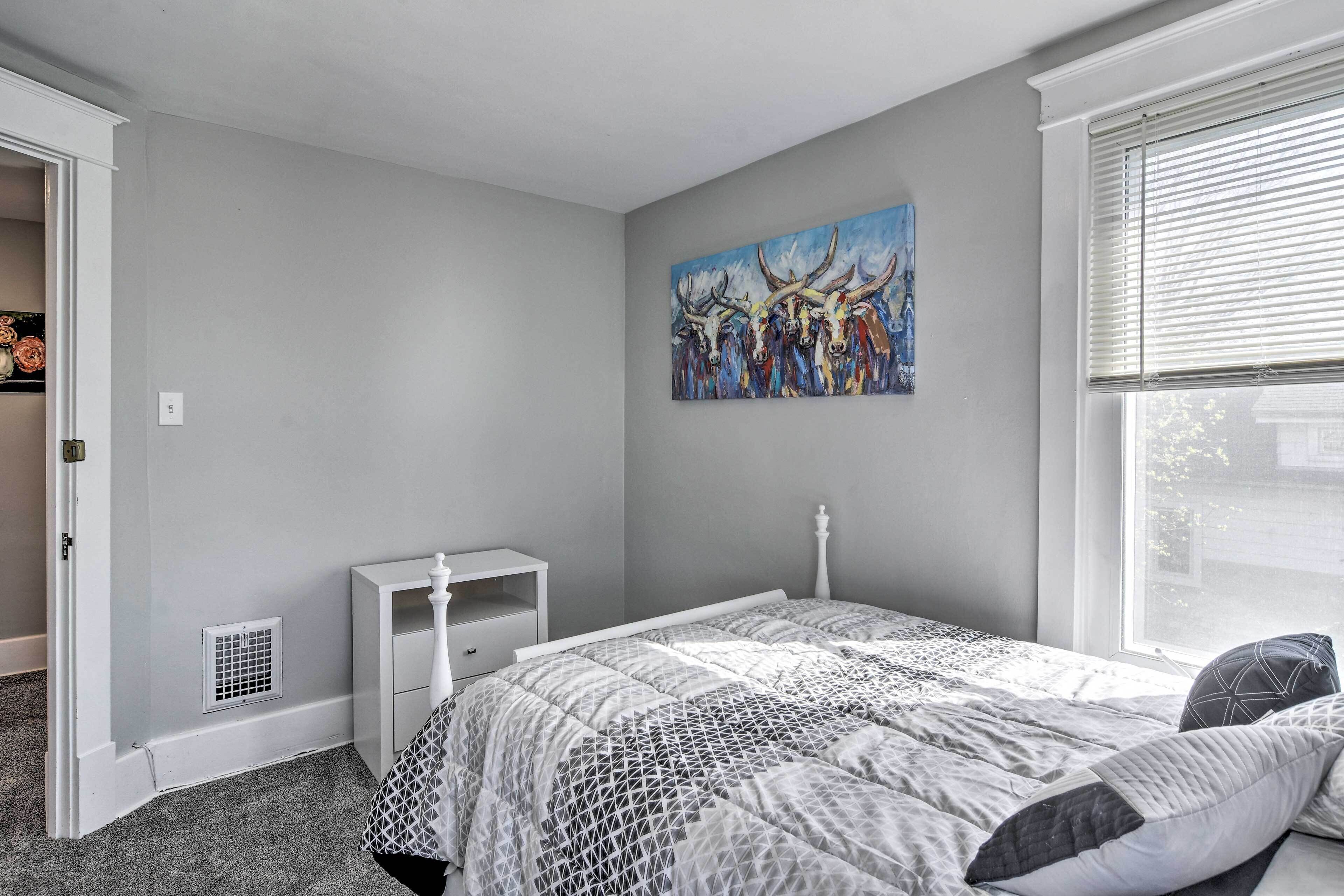 Una camera da letto con un letto, un comodino, una cassettiera, una finestra con persiane e un quadro appeso al muro.