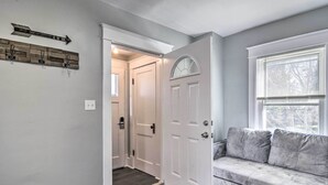 Un couloir avec une porte blanche, un canapé gris et un porte-manteau fixé au mur.