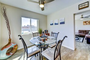 A dining area with a round glass table and chairs, a ceiling fan, and a window with a view of buildings outside. - Joshua Tree Getaway w/ Hot Tub, Pool & Fire Pit (Yucca Valley)