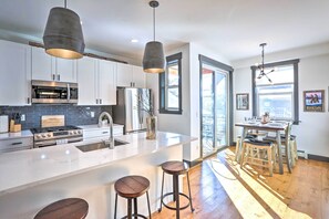 A modern kitchen with white cabinets, stainless steel appliances, a large island with stools, and a dining area with a view. - Modern Mountain Getaway, Walk to Grand Lake! (Grand Lake)