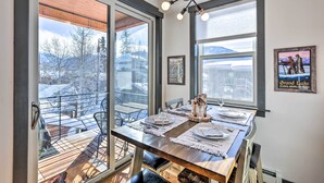 A dining area with a wooden table set for four, large windows, and a view of a snowy landscape. - Modern Mountain Getaway, Walk to Grand Lake! (Grand Lake)