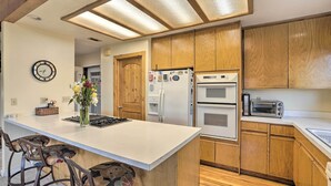 A kitchen with wooden cabinets, a white countertop, a built-in oven, a microwave, and a toaster. There is a clock on the wall and a vase with flowers on the countertop. - Homey Colfax Getaway w/ Private Hot Tub! (Colfax)