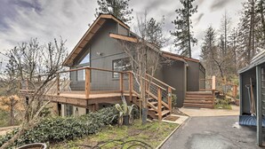 A cabin with a wooden deck, a staircase, and a large window. - Homey Colfax Getaway w/ Private Hot Tub! (Colfax)