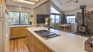 A modern kitchen with a large island, wooden cabinets, a built-in stove, and a stone accent wall. - Homey Colfax Getaway w/ Private Hot Tub! (Colfax)
