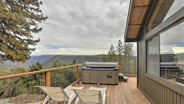 A wooden deck with two white lounge chairs, a hot tub, and a view of mountains. - Homey Colfax Getaway w/ Private Hot Tub! (Colfax)
