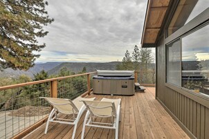 Una terraza de madera con dos sillones blancos, un jacuzzi y vistas a montañas.